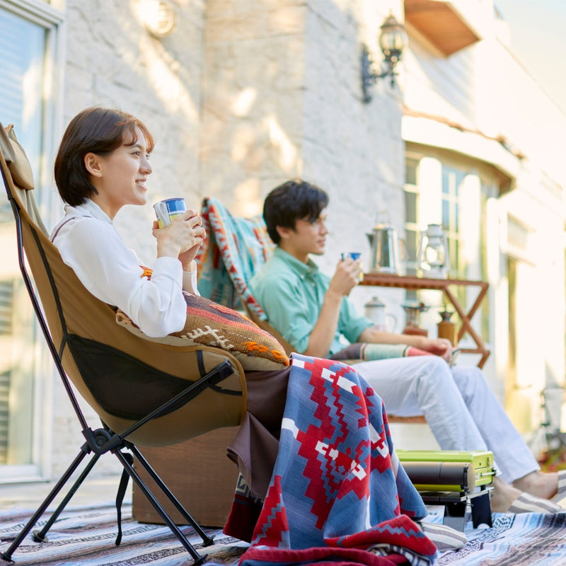 Two people sitting on a deck with a colorful blanket, enjoying drinks.