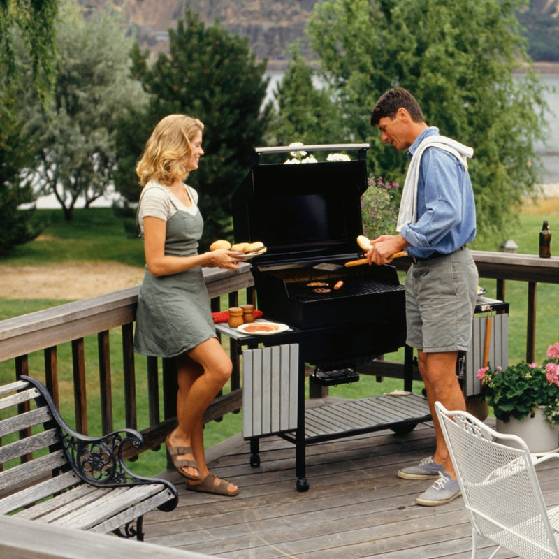 Man and woman grilling on a wooden deck with a scenic background