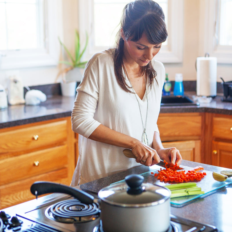 Woman chopping vegetables on a cutting board in a kitchen.